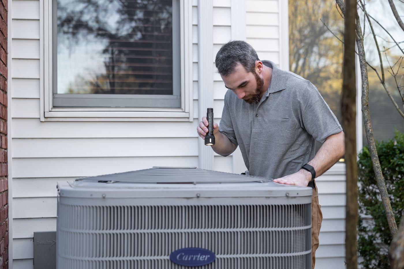 A technician checking an outdoor air conditioning unit beside a house