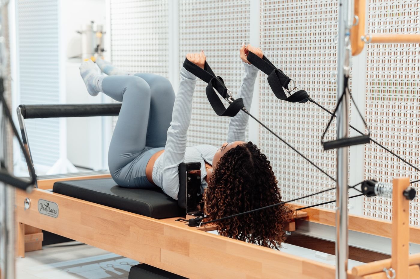 A woman exercising on a pilates reformer in a bright studio