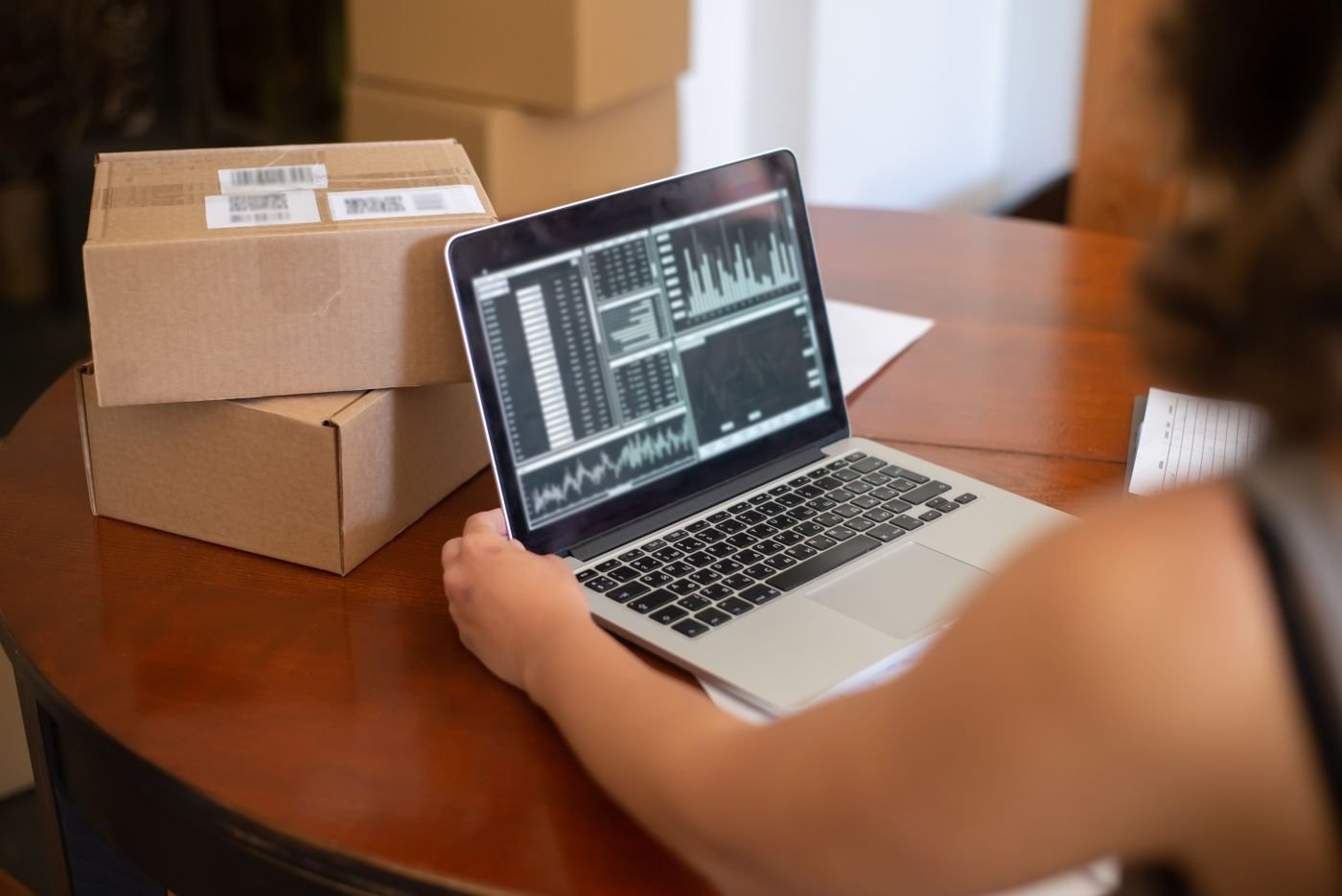 A laptop showing financial charts on a table beside shipping boxes