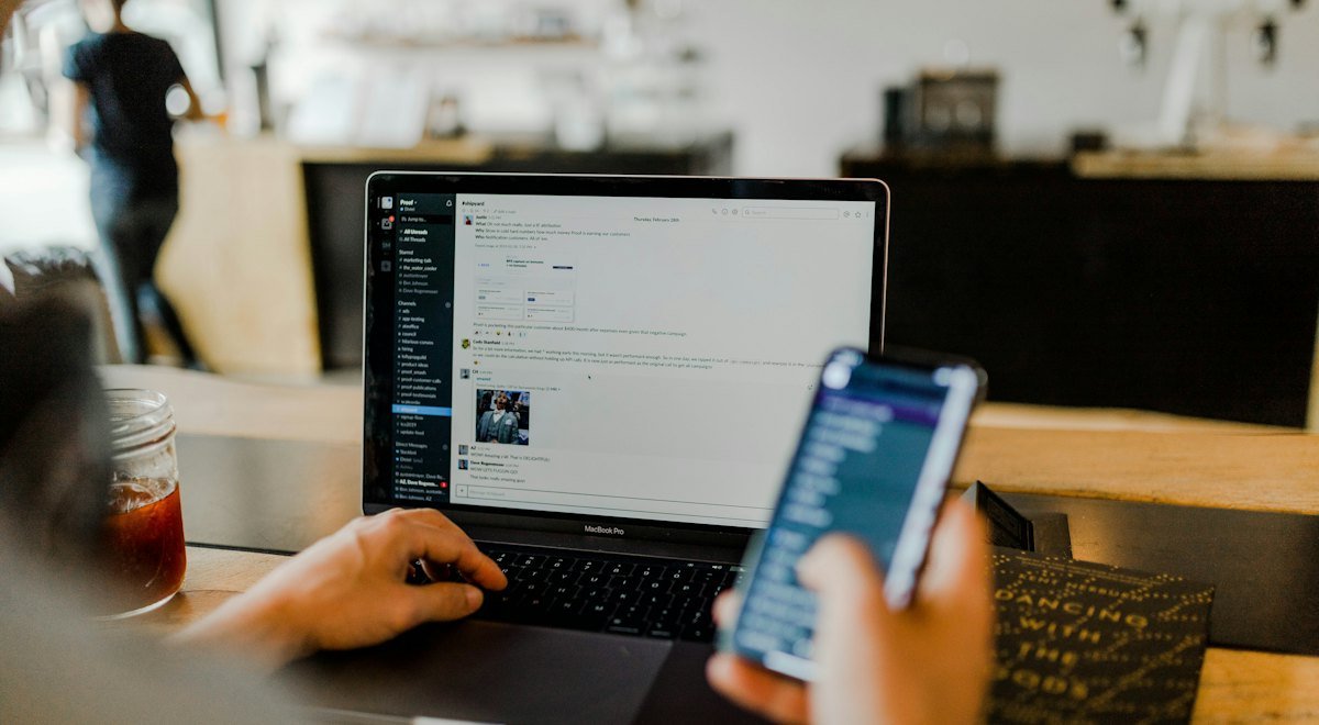 Hands on a laptop keyboard while checking a phone
