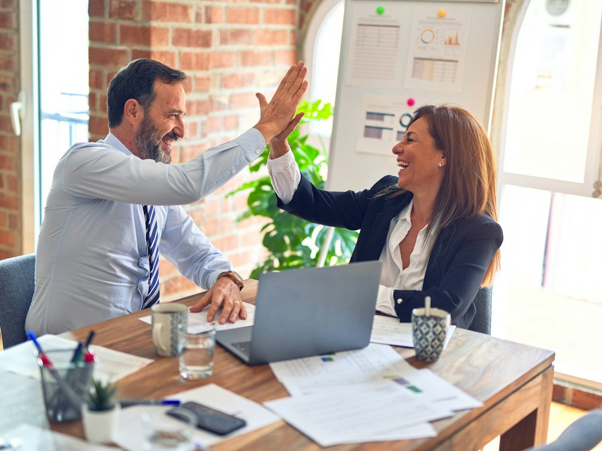 Two colleagues high-fiving across a desk after a successful project